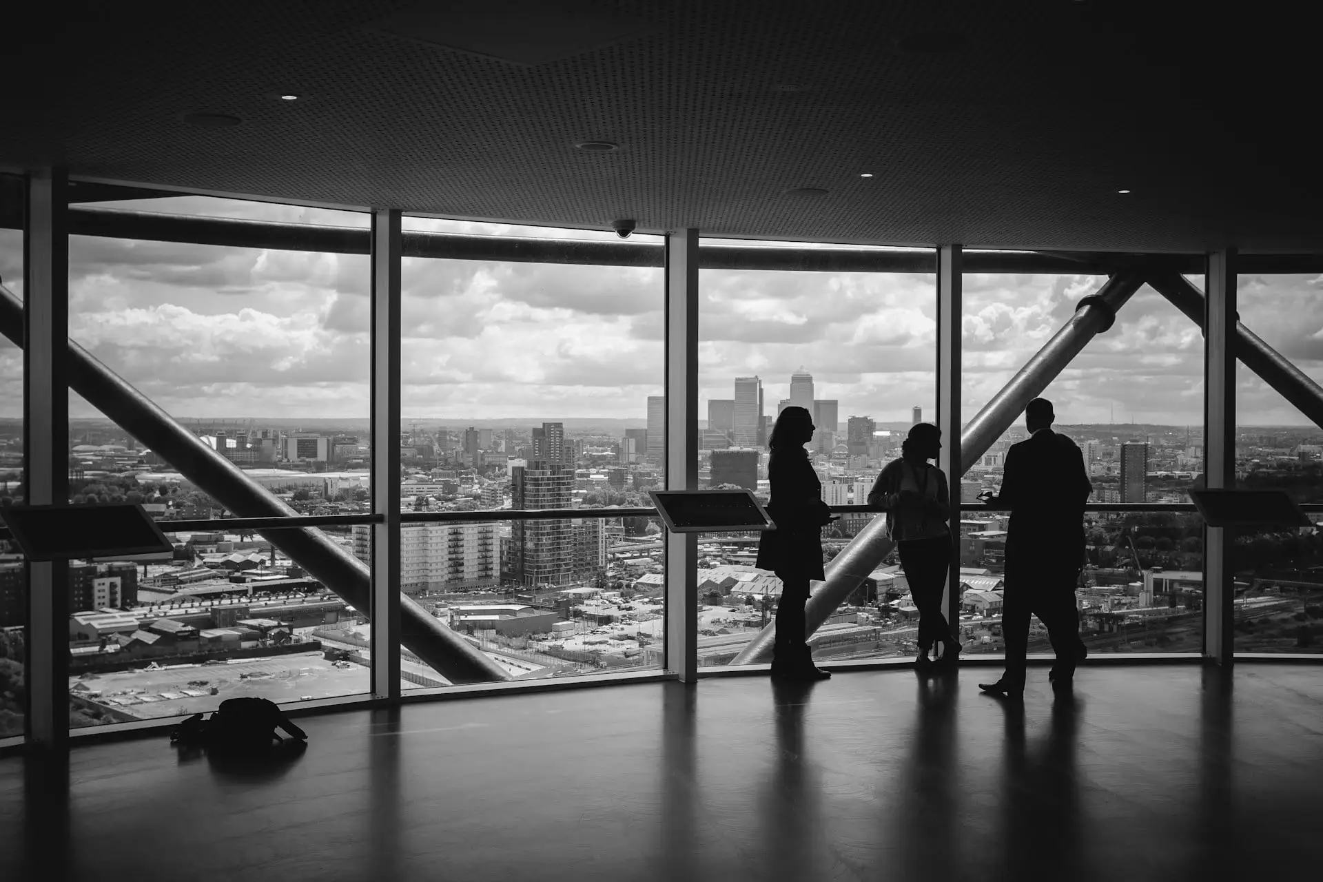 Three colleagues in silhouette at a wall of office windows, looking out over a city skyline