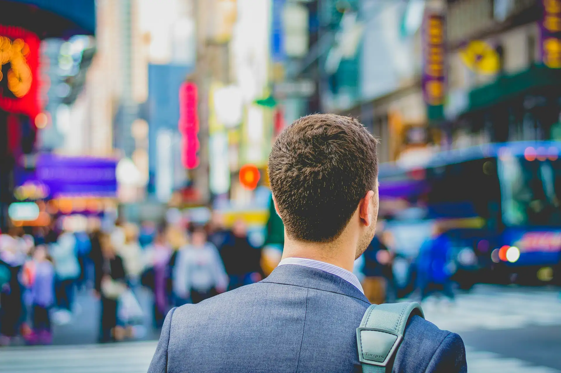 A young professional with a backpack, seen from behind on a busy city street